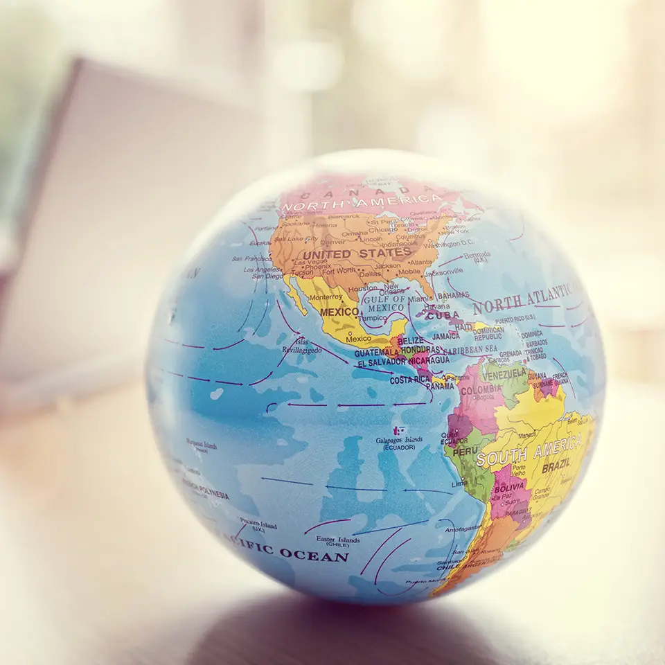 Globe in front of man's hands working at a laptop