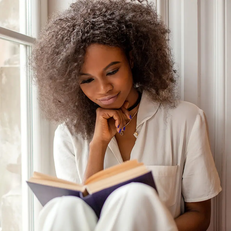 Woman sitting on a windowsill reading a book